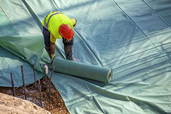 Installing plastic vapor barrier before pouring concrete slab, helping to prevent moisture from migrating up from the dirt and creating a wet slab.